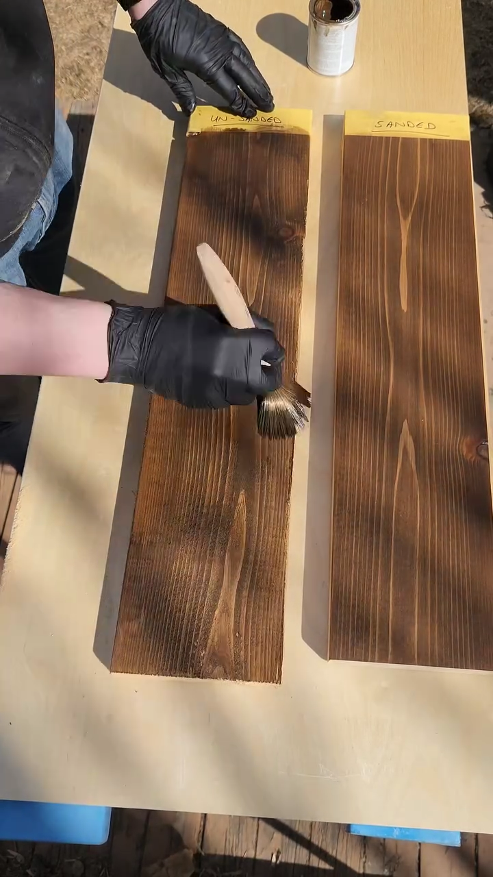 Showing the difference between applying stain on sanded wood vs unsanded wood. The sanded wood looks much nicer, someone is brushing stain on the unsanded wood.